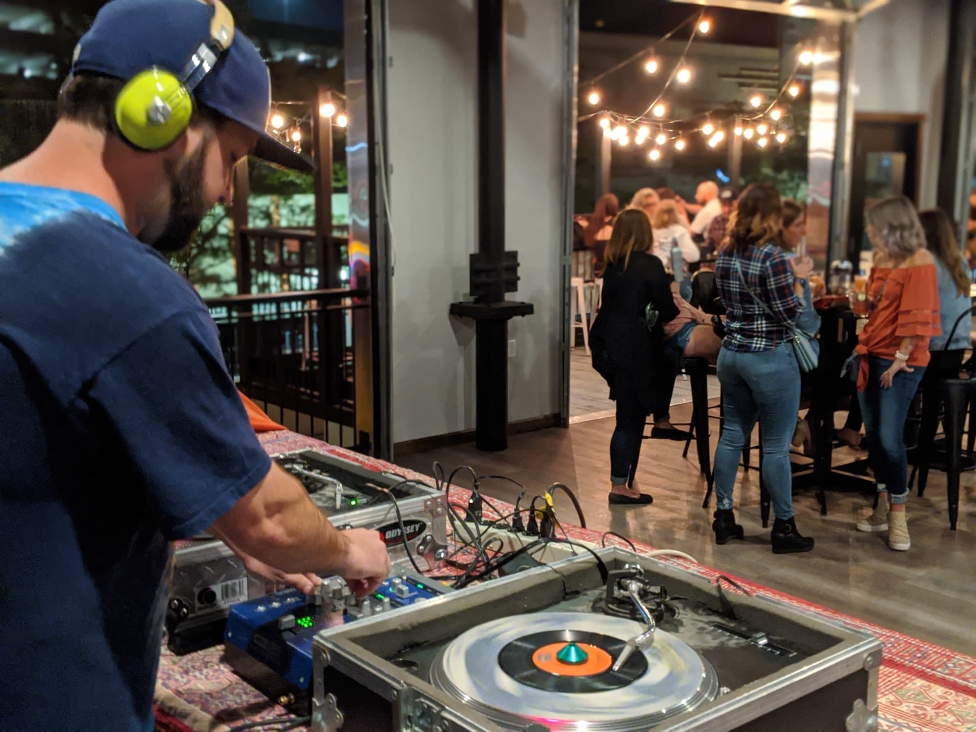 Casey Green playing a 45 on Technics turntables while a crowd talks under string lights